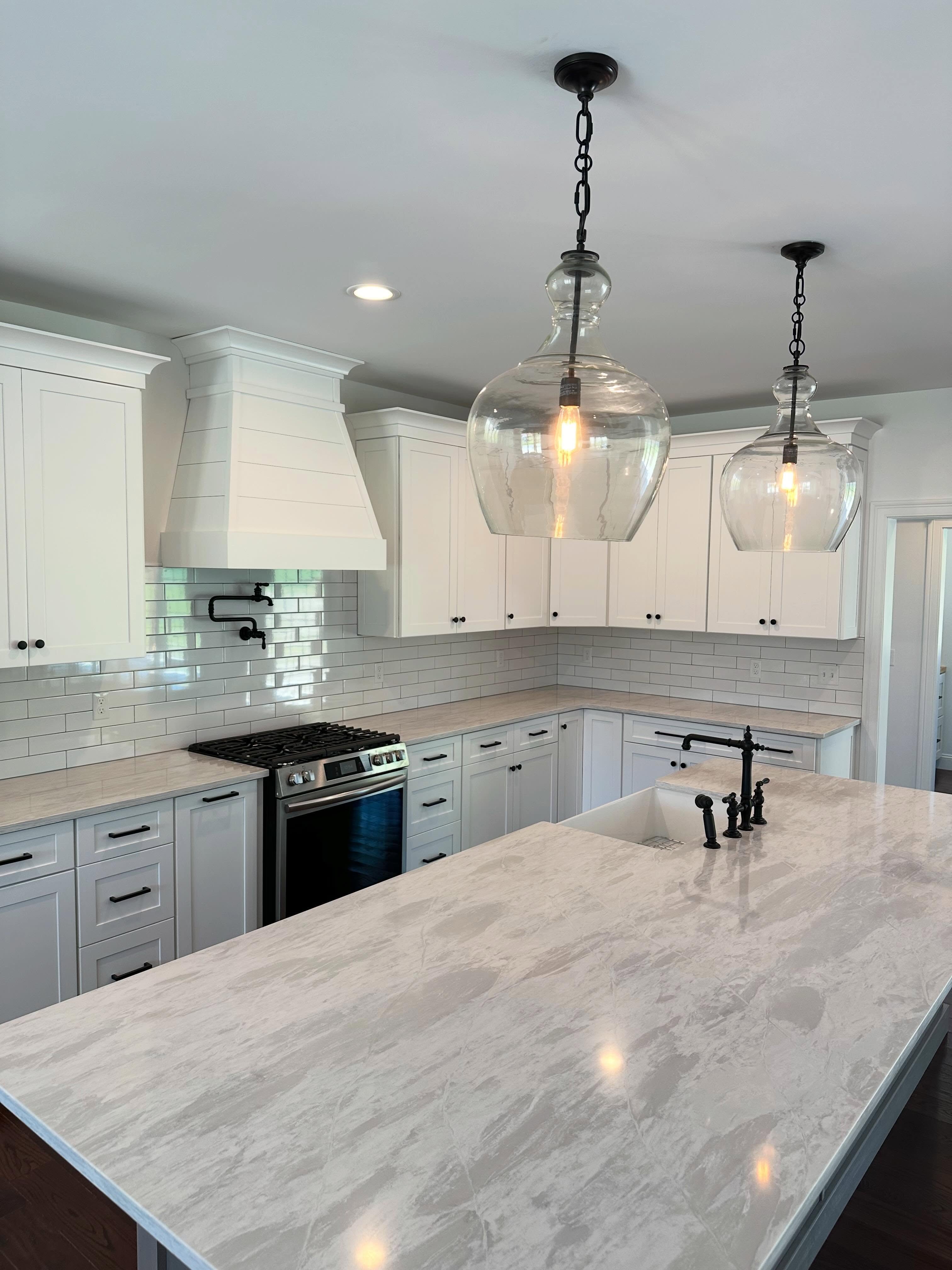 White kitchen with glass pendant lights and marble-topped island